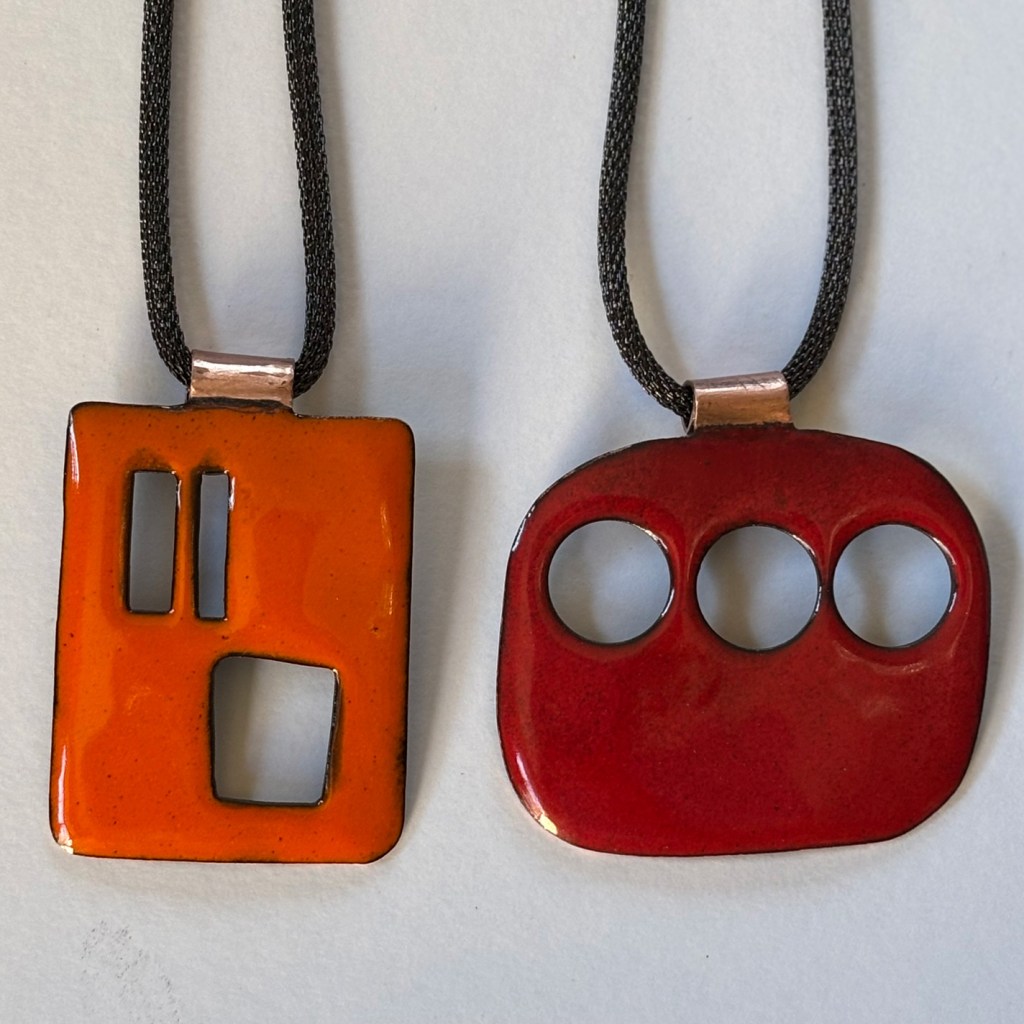Photo of two artistic enamel pendants in red and orange