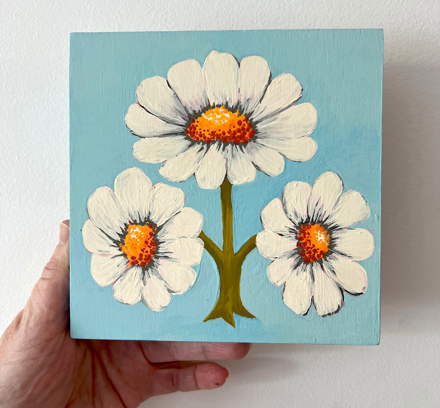 Photo of painting being held in a hand depicting flowers on a blue background
