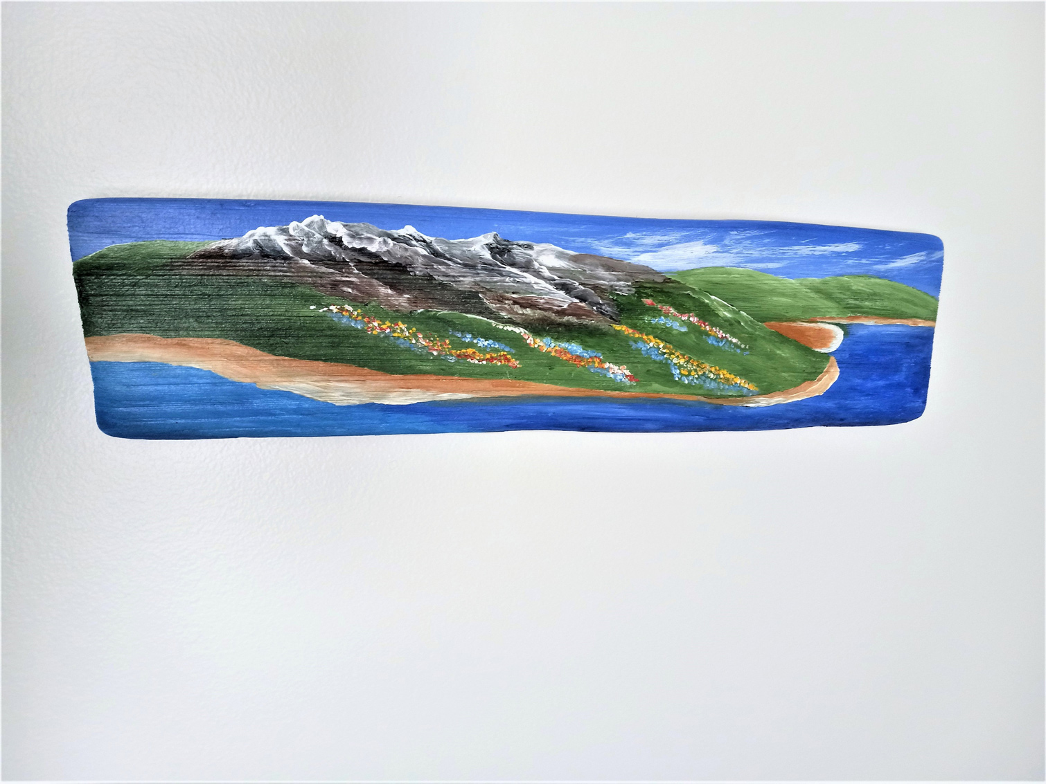 Painting on driftwood showing scenic landscape of mountains and water