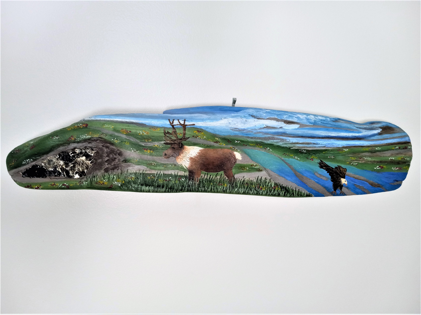 Painting on driftwood showing caribou and eagle in scenic landscape