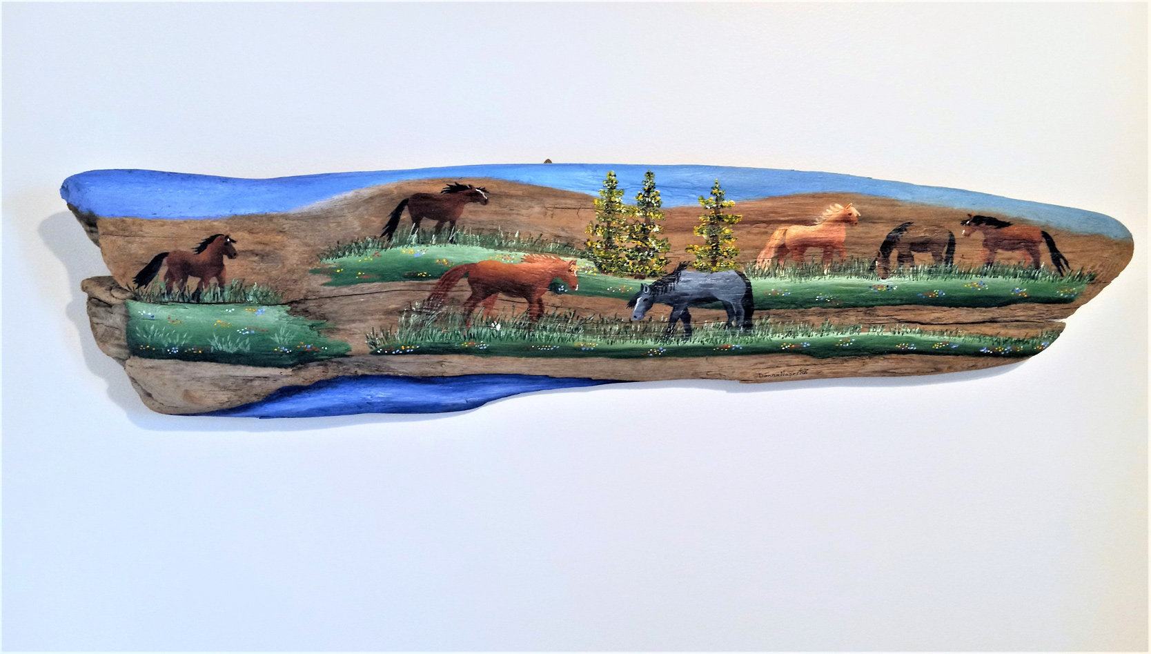 Painting on driftwood showing horses in field with water in foreground