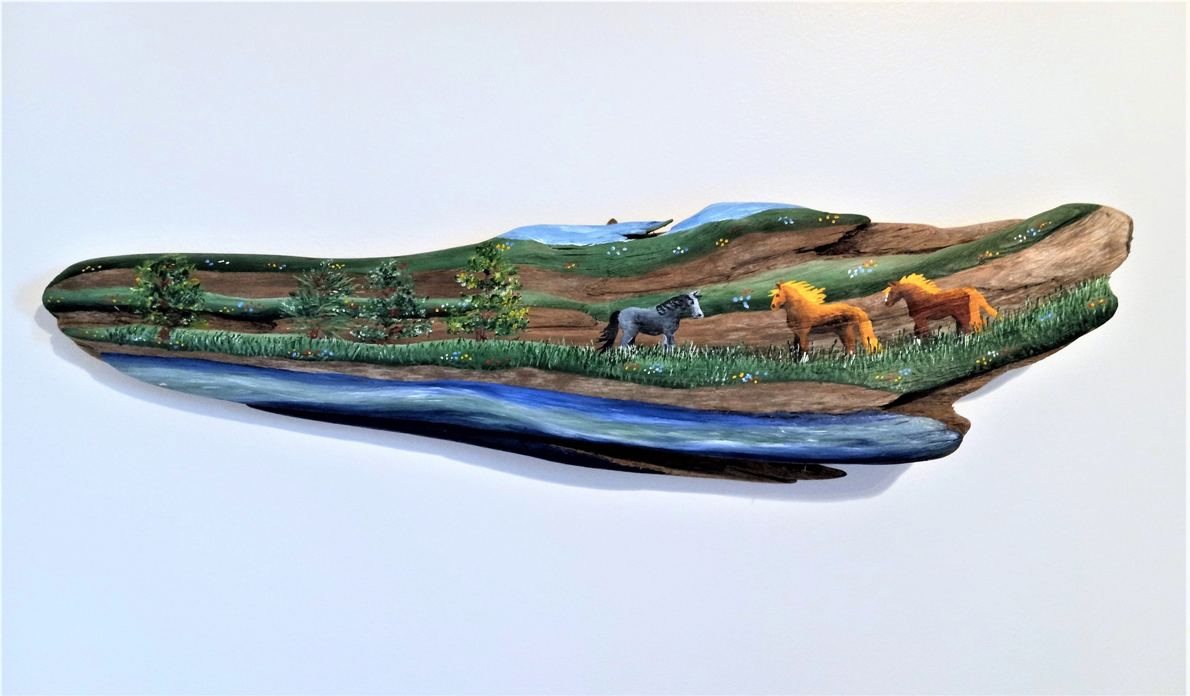 Painting on driftwood showing horses in field with water in foreground