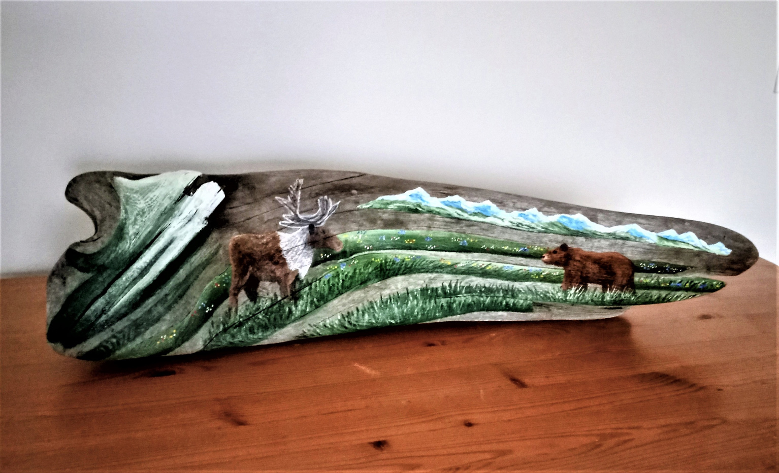Painting on driftwood showing caribou and grizzly bear against mountain range