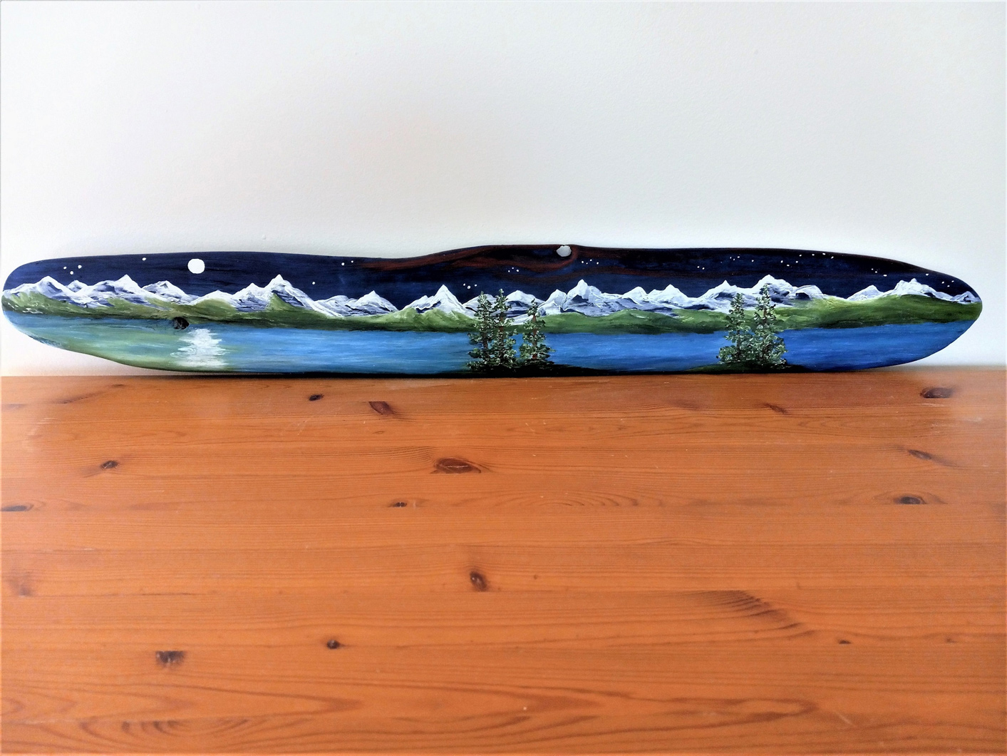 Painting on driftwood showing nighttime mountain range and water