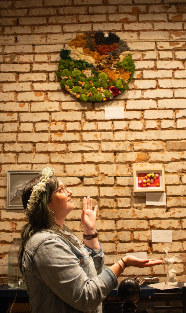 Photo of Kayla Spagnoli looking at artistic moss creation hanging on wall