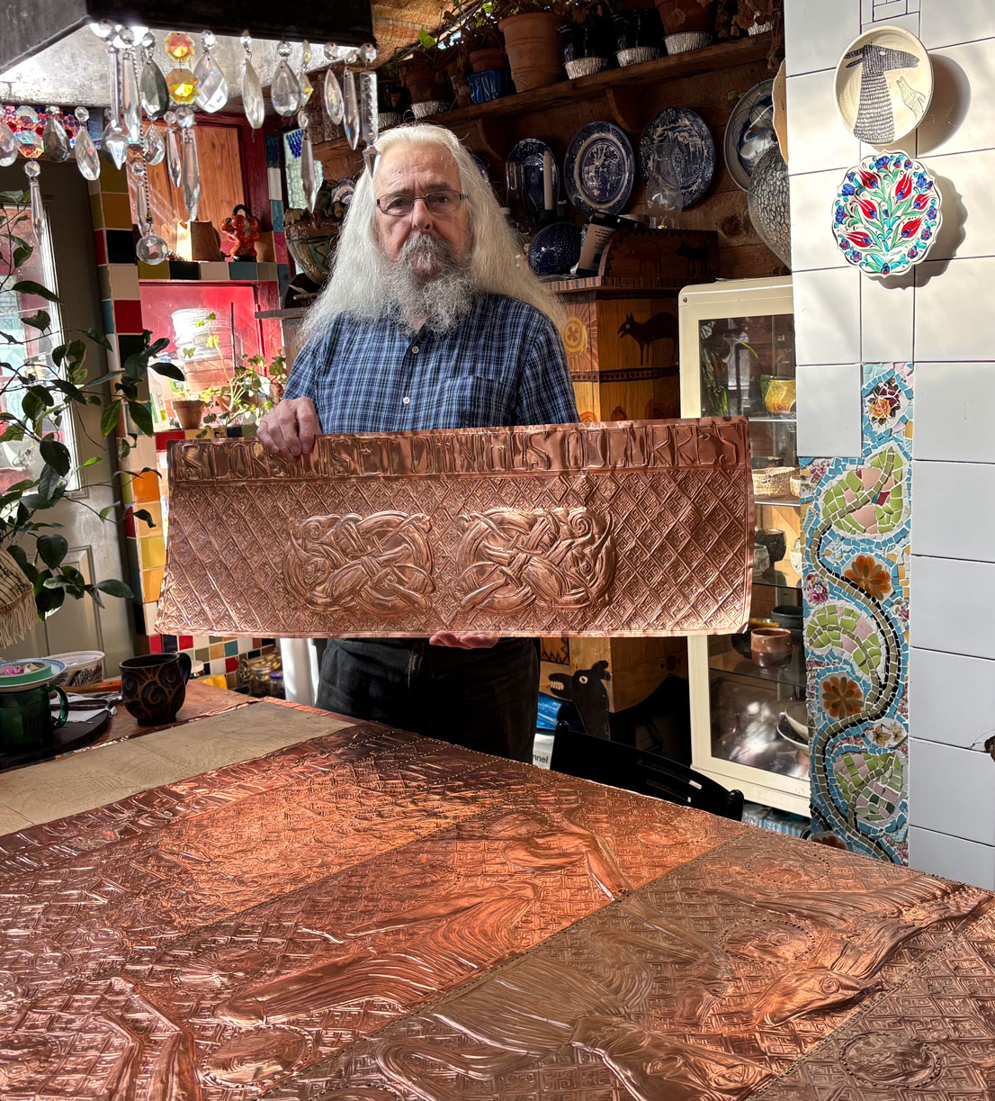 Photo of artist Robert Pauly holding hand-beaten copper door panel